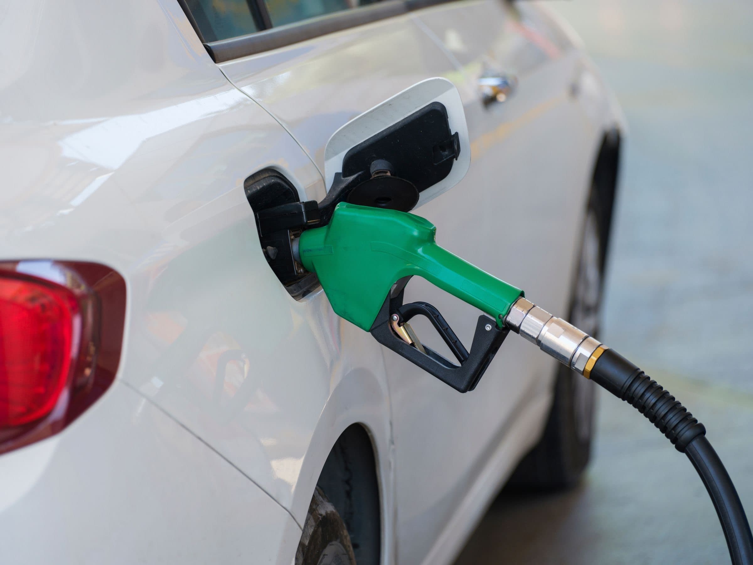 A green fuel nozzle filling a white car